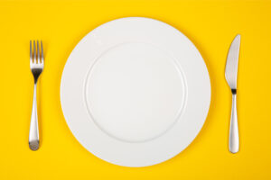 Aerial view of a white plate on a yellow background that will hold foods to eat after oral surgery