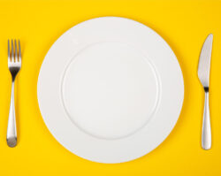 Aerial view of a white plate on a yellow background that will hold foods to eat after oral surgery