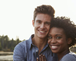 Black and white couple smiles while embracing outside