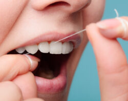 Closeup of a woman string flossing between her teeth against a blue background