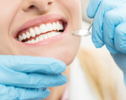 Closeup of a woman smiling at the dentist during her dental cleaning with blue gloved hands examining her mouth with a special dental mirror