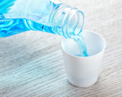 Blue mouthwash being poured into a white cup from a clear bottle