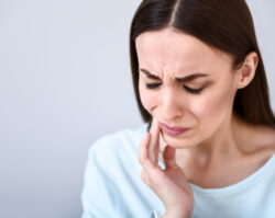 Brunette woman cringes in pain and touches her cheek due to sensitive teeth